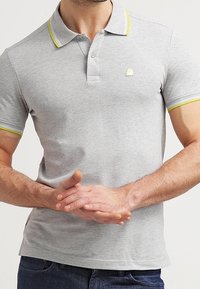 Grå polo skjorta i bomull, med en treknapps placket, gula detaljer på kragen och ärmarna, samt en liten logga på bröstet.