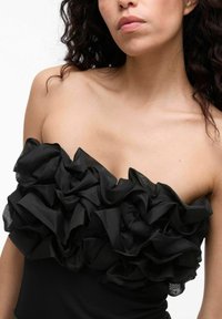 Czarny top bez ramiączek z falbaniastej struktury, z warstwowym przezroczystym materiałem. Dopasowany krój podkreśla górną część ciała.