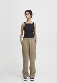 Svart ärmlös topp och beige cargobyxor med elastisk midja. Byxorna har sidofickor. Modellen bär svart och vita sneakers.