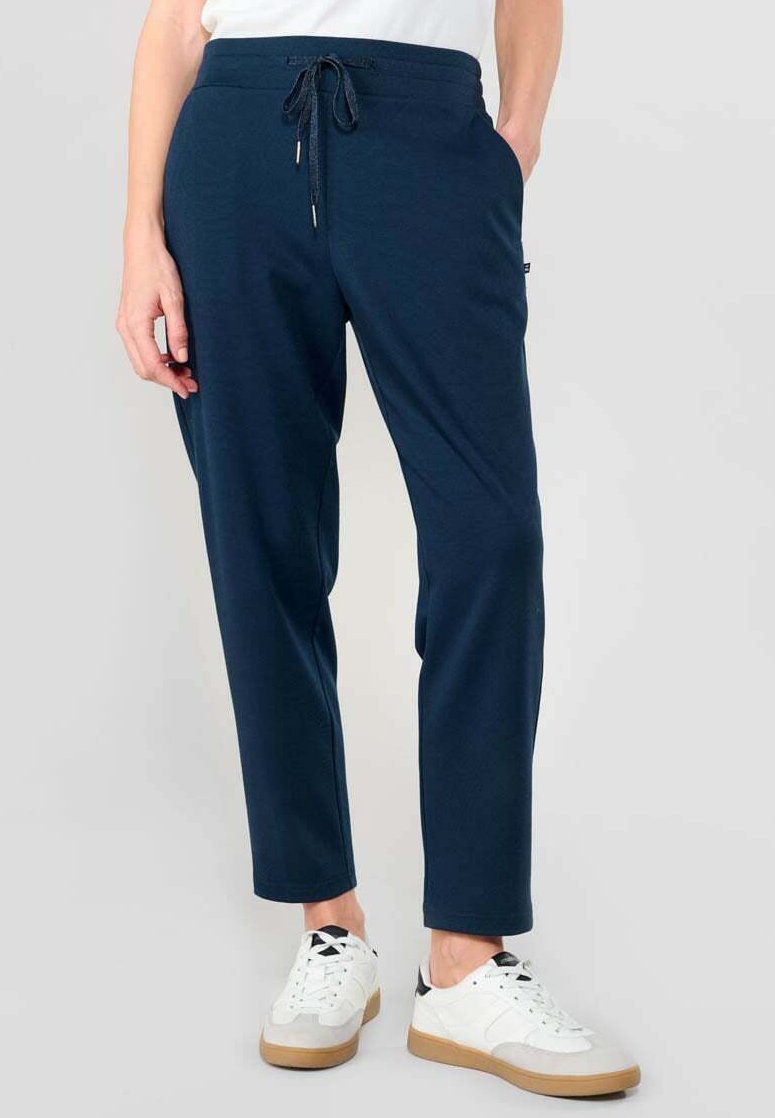 Pantalones jogger azul marino con cinturilla elástica, cordón y bolsillos laterales; combinados con zapatillas blancas con detalles en gris y negro.