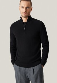 Czarny sweter z dzianiny z suwakiem przy szyi, wyposażony w prążkowany dół i mankiety. Połączony z szarymi, dopasowanymi spodniami.