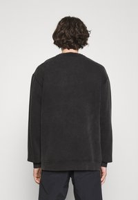 Felpa nera oversize con maniche lunghe, scollatura rotonda e finitura testurizzata. Presenta un orlo e polsini a costine per un tocco di dettaglio in più.
