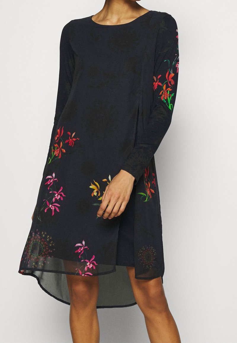 Robe noire à manches longues, ornée d'une broderie florale colorée. Ourlet arrière un peu plus long avec une texture subtile. Tissu lisse.