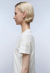 Witte katoenen t-shirt met ronde halslijn en korte mouwen, voorzien van een gemêleerd logo-patch op de linker mouw. Soepele stofstructuur.