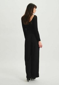 Haut noir à manches longues avec un dos décolleté, associé à un pantalon noir à jambes larges. La tenue présente un tissu lisse et une silhouette ajustée.