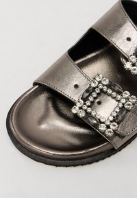 Tongs en métal gris avec deux larges brides et un cluster décoratif de gemmes claires et noires sur le devant. Semelle intérieure texturée.