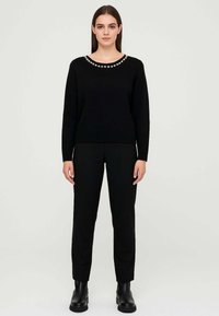 Maglione nero a maglia con scollo rotondo decorato con perline. Abbinato a pantaloni neri e stivaletti alla caviglia. Texture liscia.