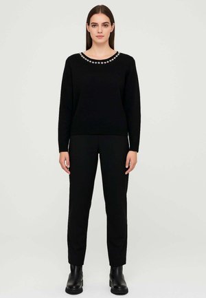 Maglione nero a maglia con scollo rotondo decorato con perline. Abbinato a pantaloni neri e stivaletti alla caviglia. Texture liscia.