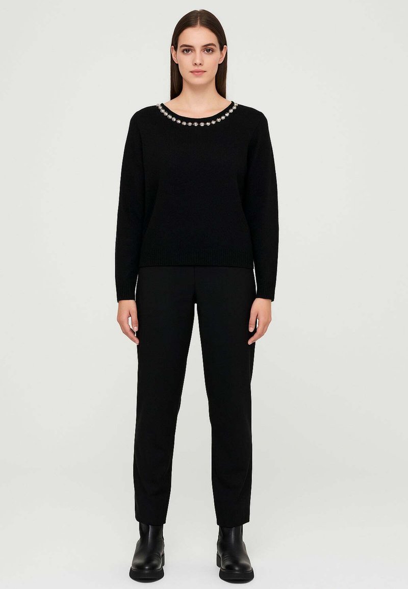Maglione nero a maglia con scollo rotondo decorato con perline. Abbinato a pantaloni neri e stivaletti alla caviglia. Texture liscia.
