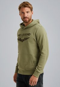 Olive green hoodie made of cotton, featuring a front kangaroo pocket, ribbed cuffs, and a graphic print with wings and text on the chest.