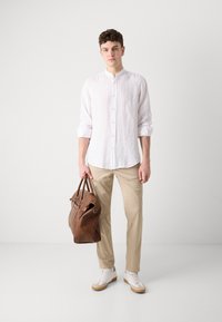 Lichtgewicht wit linnenshirt met een staande kraag, beige broek, bruine leren tas en witte sneakers met beige accenten.