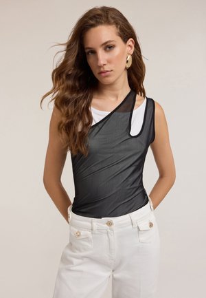 Un haut sans manches en noir transparent avec une couche intérieure blanche, présentant un col diagonal et un matériau léger, associé à un pantalon taille haute blanc.