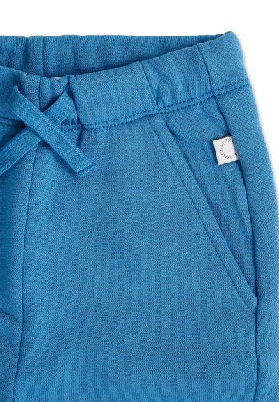 Pantalons de survêtement en coton bleu avec une taille élastique, un cordon de serrage, des poches latérales et une petite étiquette sur la taille. Texture lisse.