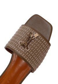 Sandal à glissière marron avec une lanière texturée ornée de surpiqûres diagonales et d'un accent doré. Bout carré et semelle plate.