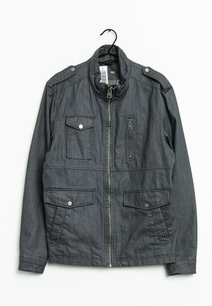 Giacca casual grigio scuro con cerniera frontale, quattro tasche frontali di cui una con cerniera, e mostrine sulle spalle su gruccia nera.