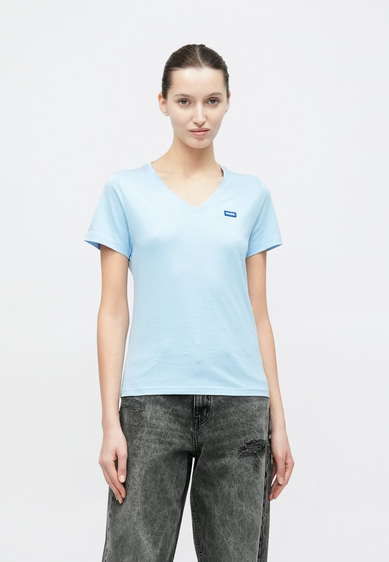 Ανοιχτό γαλάζιο μπλουζάκι με λαιμόκοψη σε σχήμα V, κατασκευασμένο από απαλό βαμβακερό ύφασμα, με κοντά μανίκια και μικρό μπλε λογότυπο στην αριστερή πλευρά του στήθους.