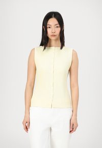 Light yellow sleeveless top with a fitted design, ribbed texture, and a button-up front. White pants complement the top's color.