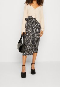 Cardigan en ribbed beige avec des boutons, associé à une jupe midi noire avec un motif d'étoiles dorées et une taille froncée. Sac noir et chaussures à plateforme.