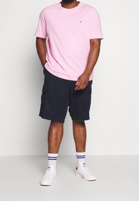 Camiseta de algodón rosa claro con mangas cortas y un pequeño logo; pantalones cortos cargo azul marino con bolsillos laterales; zapatillas blancas con detalles negros y calcetines de rayas.