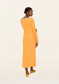 Langärmliges, knöchellanges Kleid in lebhaftem Orange mit einem kontrastierenden marineblauen Ausschnitt. Verfügt über seitliche Schlitze und eine taillierte Silhouette.
