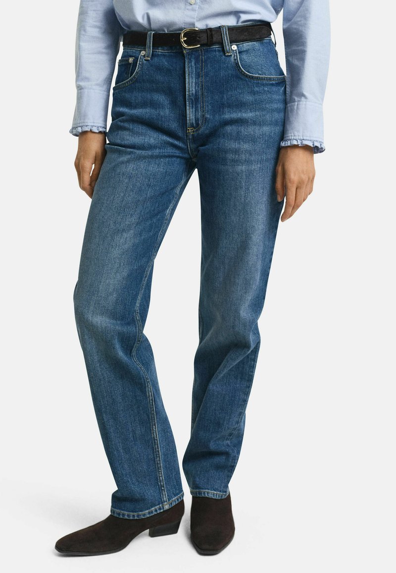 Blå denimjeans med avslappnad passform, hög midja och två framfickor. Bärs med ett svart bälte och bruna klackstövlar.