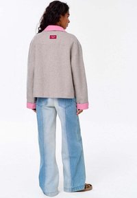 Šedá vlna smíchaná bunda s růžovým límcem a manžetami, se červenou nášivkou na zadní straně. Vhodná k světle modrým širokým džínům.