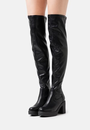 Bottes en cuir noir montantes au-dessus du genou avec une texture lisse, un talon épais et un détail de couture latérale. Le design se caractérise par une jambe ajustée et un bout arrondi.