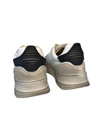 Sneakers bianchi con suola grigia testurizzata, dettaglio nero sul tallone e design curvo. La parte superiore è in pelle liscia con un tallone in gomma a contrasto.