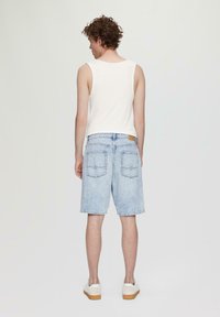 Hemdblauwe denim shorts met een relaxte pasvorm, twee achterzakken en een label op de tailleband, gecombineerd met een witte mouwloze top.