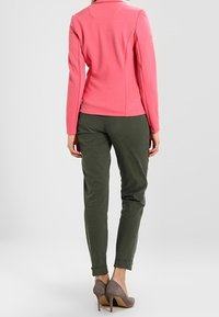 Haut rose texturé à manches longues, pantalon fuselé vert olive, et chaussures à talons gris. Accent sur un design épuré et une silhouette ajustée.