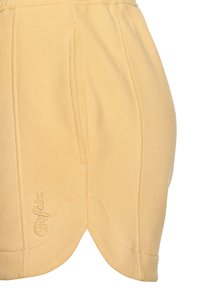 Helle gelbe Shorts aus weichem Stoff mit gewelltem Saum, ausgestattet mit Fronttaschen und gesticktem Logo-Detail an der Seite.