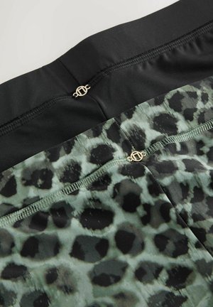 Mustade ja roheliste leopardimustriliste retuuside sile tekstuur. Vöökoha juures on õmblused ja kuldsed riistvara detailid.