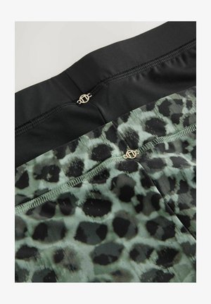 Mustade ja roheliste leopardimustriliste retuuside sile tekstuur. Vöökoha juures on õmblused ja kuldsed riistvara detailid.