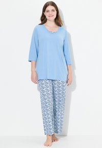 Lichtblauw pyjama set met een langslavige top en een ronde hals, en een broek met een blauw-witte golfpatroon. Zachte stof, relaxte pasvorm.