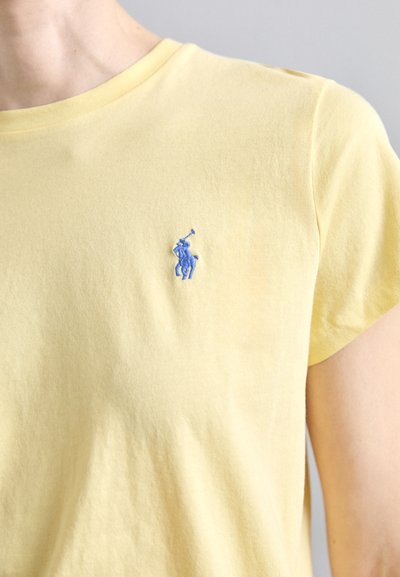 Dzeltena kokvilnas T-krekls ar klasisko apkakli un īsām piedurknēm. Uz kreisā krūšu daļas izšūts zils polo spēlētāja logo.