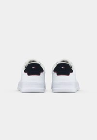 Paire de baskets blanches avec des patchs noirs au talon et un petit logo rouge, blanc et bleu à l'arrière, placées côte à côte sur un fond blanc.