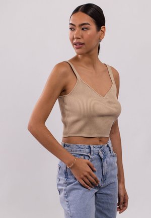 Beige geripptes Crop-Top mit V-Ausschnitt und dünnen Trägern, kombiniert mit hellblauen, hochgeschnittenen Jeans. Glatte Textur und taillierte Form.