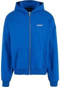 Blaue Kapuzenjacke mit Reißverschluss aus weichem Material, ausgestattet mit einer Kängurutasche und gerippten Bündchen. Weißer Logo-Text auf der Brust sorgt für Details.