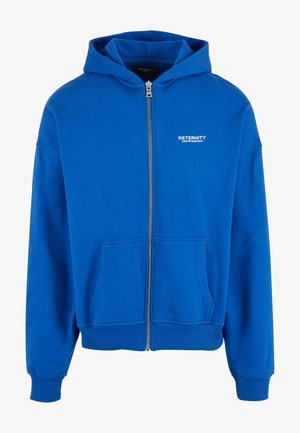 Kék cipzáros kapucnis pulóver, puha anyagból készült, kenguru zsebbel és bordázott mandzsettákkal rendelkezik. A mellkason lévő fehér logós szöveg részletgazdagabbá teszi.