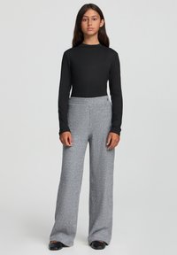 Czarna bluzka z długim rękawem w połączeniu z szerokimi, prążkowanymi, szarymi spodniami. Gładka tekstura materiału z wysokim stanem. Czarne buty.