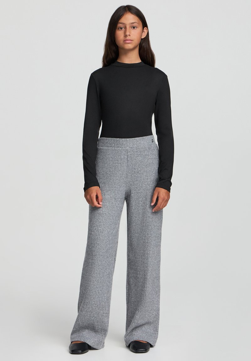 Czarna bluzka z długim rękawem w połączeniu z szerokimi, prążkowanymi, szarymi spodniami. Gładka tekstura materiału z wysokim stanem. Czarne buty.