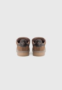 Brown suede sneakers with a textured finish, padded tongues, and a rubber sole. Features a dark logo on the heel and simple stitching.