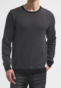 Sweat-shirt noir avec un motif à pois, col rond, et poignets et ourlet côtelés. Fait en tissu doux avec une finition texturée.