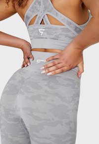 Gray sports bra and leggings with a subtle camo pattern. Material appears stretchy with crossed back straps and logo accents.