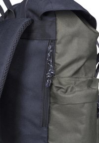 Sac à dos noir et vert olive avec une sangle en mesh, des zips et une poche latérale pour un rangement supplémentaire. Texture de tissu durable.