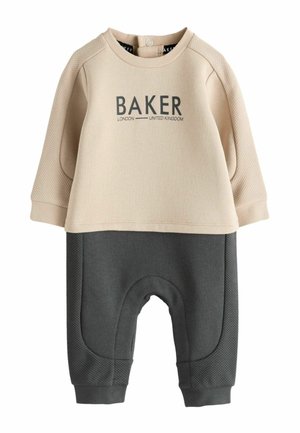 Top bej cu mâneci lungi cu textul „BAKER London United Kingdom” asortat cu pantaloni gri închis având panouri laterale texturate și manșete.