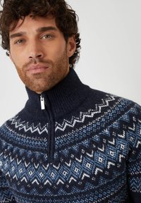 Granatowy sweter z dzianiny z wysokim kołnierzem, z geometrycznymi wzorami w odcieniach niebieskiego i białego, z zapięciem na zamek błyskawiczny przy szyi.