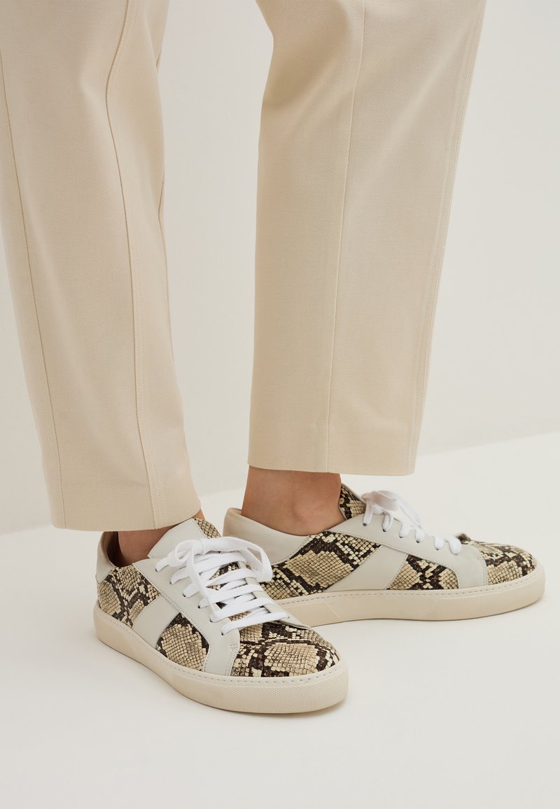 Sneaker mit einem Obermaterial in Beige und schwarzem Schlangendruck, weißen Schnürsenkeln und einer hellen Sohle. Entworfen mit einem kontrastierenden Seitenpaneel.