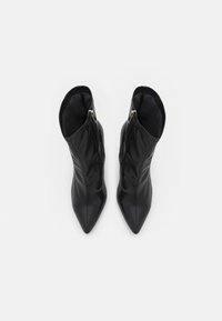 Bottines noires en cuir lisse avec un bout pointu et une fermeture à glissière, présentant des coutures verticales subtiles pour ajouter de la texture.