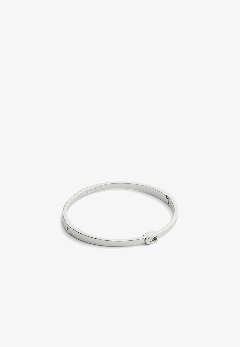 Brazalete de metal plateado con un diseño circular liso, un mecanismo de cierre simple y un logo de marca grabado.